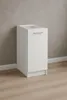 A white kitchen base cabinet with a silver handle stands against a textured gray wall and a light wood floor. Produktbild-Vorschau