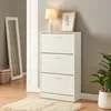 A white shoe cabinet with three drawers is shown in a room with a mirror and a plant. Anteprima dell’immagine prodotto