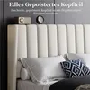A close-up view of a bed with a white upholstered headboard, featuring pillows and a decorative throw blanket. Produktbild-Vorschau