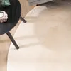 A close-up view of a round, cream-colored fluffy rug next to a black side table with a candle and a plant. Produktbild-Vorschau