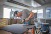 A man is using a jigsaw to cut a piece of material on a workbench in what appears to be a workshop or construction site. Anteprima dell’immagine prodotto