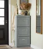 A gray shoe cabinet with three flip drawers is shown in a hallway next to a black door and a mirror. Podgląd zdjęcia produktu