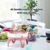 A knitting machine and various yarn balls are arranged on a table, with a plant in the background. Náhled obrázku produktu