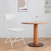 A white folding chair is placed next to a round wooden table with two glasses and a bottle of water on it, in a room with white walls and wooden flooring. Anteprima dell’immagine prodotto