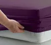 A hand is shown tucking a purple fitted sheet onto a mattress. Produktbild-Vorschau