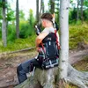 A person with a backpack sitting on a tree stump in a forest. Anteprima dell’immagine prodotto