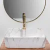 A rectangular marble-patterned sink with a gold faucet in front of a round mirror. Náhľad obrázku produktu
