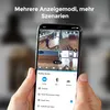 A person is holding a smartphone displaying a multi-camera view from a security system. Produktbild-Vorschau