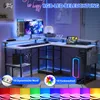 A modern L-shaped gaming desk with RGB LED lighting, multiple monitors, a computer tower, and accessories. Náhled obrázku produktu