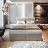 A luxurious bedroom with a large boxspring bed as the focal point, decorated with plush pillows and throws. The room features modern lighting and elegant wall paneling. Voir les images du produit