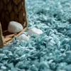 A close-up of a fluffy blue rug with three white stones and a woven basket. Produktbild-Vorschau