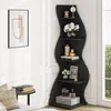 A black, wave-shaped corner shelf unit is filled with decorative items in a room. Podgląd zdjęcia produktu