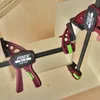 Two clamps are shown holding together wooden pieces, likely in a woodworking or DIY setting. Náhled obrázku produktu