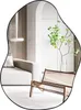 A modern living room with a couch, chair, and a plant reflected in an asymmetrical mirror. Produktbild-Vorschau