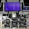 Three suitcases are lined up in an airport terminal in front of a departure board. Produktbild-Vorschau