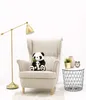 A plush panda toy with its baby sits on a beige armchair next to a small side table with decorative items. Podgląd zdjęcia produktu