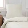 A close-up view of a cream-colored duvet and pillow on a bed, with a woven basket in the background. Produktbild-Vorschau