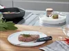 A cooked steak on a plate with a thermometer, near cooking utensils and ingredients. Anteprima dell’immagine prodotto