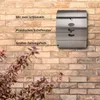 A silver mailbox mounted on a brick wall, with text overlays highlighting its features. Produktbild-Vorschau