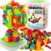 A collection of colorful building blocks, some assembled into a castle-like structure, and others loose in a clear plastic container. Voir les images du produit