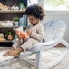 A young child sits in a rocking chair holding a stuffed animal. Produktbild-Vorschau
