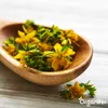 A wooden spoon filled with yellow flowers and green leaves, with a few flowers scattered on a white wooden surface. Náhľad obrázku produktu