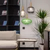 A living room scene with a sofa, coffee table, bookshelves, and a plant, featuring three pendant lights. Produktbild-Vorschau