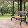 A wooden and metal garden bench sits on a wooden deck, with a park-like setting visible through large windows behind it. Produktbild-Vorschau