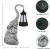 A solar-powered elephant garden decoration holding a lantern, with close-up views of its features and dimensions. Produktbild-Vorschau