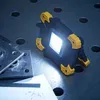 A work light is placed on a metal surface with some blueprints and metal plates. Produktbild-Vorschau