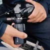 A person's hands are holding a black electric fishing reel and a black battery pack with blue indicator lights. Náhled obrázku produktu