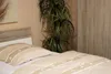 A bed with a duvet and a pillow in a room with a plant and a wardrobe. Produktbild-Vorschau