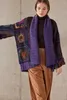A woman wearing a colorful crocheted cardigan and a purple scarf, standing against a gray wall. Produktbild-Vorschau