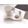 A white ceramic coffee cup and saucer with a cookie and spoon on a white surface. Produktbild-Vorschau