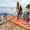 A man is pumping up an inflatable stand-up paddleboard on a beach. Produktbild-Vorschau
