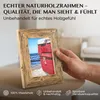 A hand holding a wooden picture frame with a photo of a red boat on a beach inside. The frame is placed on a table. Text overlays describe the product's features. Produktbild-Vorschau