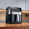 A black and silver air fryer sits on a wooden table in a kitchen setting. Náhled obrázku produktu