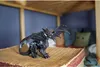 A toy dragon figurine is placed on a textured surface, with a bed and pillows visible in the background. Voir les images du produit