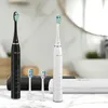 Two electric toothbrushes, one black and one white, are displayed on a marble countertop with two replacement brush heads in front of them. A white charging case is also visible. Produktbild-Vorschau