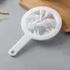 A white mesh strainer with a handle rests on a grey surface next to a wooden board. Produktbild-Vorschau