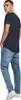 A man wearing a dark blue t-shirt and light blue jeans, posing with his hands in his pockets. Produktbild-Vorschau
