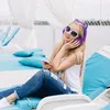A young woman wearing headphones with cat ears and sunglasses is relaxing on a blue lounge chair outdoors, holding a smartphone. Náhľad obrázku produktu