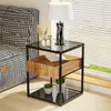 A bedside table with a drawer and shelves is placed next to a bed with a houndstooth pattern. A lamp sits on top of the table. Produktbild-Vorschau