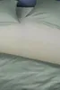 A close-up view of a bed with light green bedding and pillows. Produktbild-Vorschau