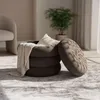 A round ottoman with a blanket and pillow inside, placed on a patterned rug in a well-lit room. Produktbild-Vorschau