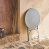A round bistro table is folded and leaning against a textured wall, with a lantern and dried reeds nearby. Anteprima dell’immagine prodotto