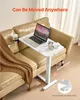 A white adjustable laptop table with a laptop, headphones, and a mouse on it, placed next to a tan leather couch with a brown blanket draped over it. Produktbild-Vorschau