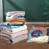Transparenter Vakuum-Aufbewahrungsbeutel mit blauem Ventil, gefüllt mit komprimierter Kleidung, neben einem hohen Stapel unkomprimierter gefalteter Kleidung Náhled obrázku produktu