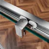 Close-up of a shower door roller mechanism on a glass panel, with a wooden floor in the background. Produktbild-Vorschau