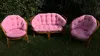 Three pieces of rattan furniture with pink cushions are placed on a grassy lawn. Produktbild-Vorschau